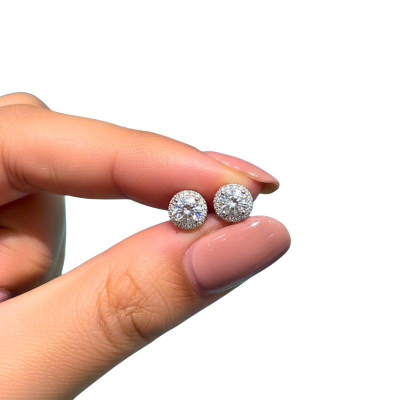 Diamond earrings held between fingers on a white background