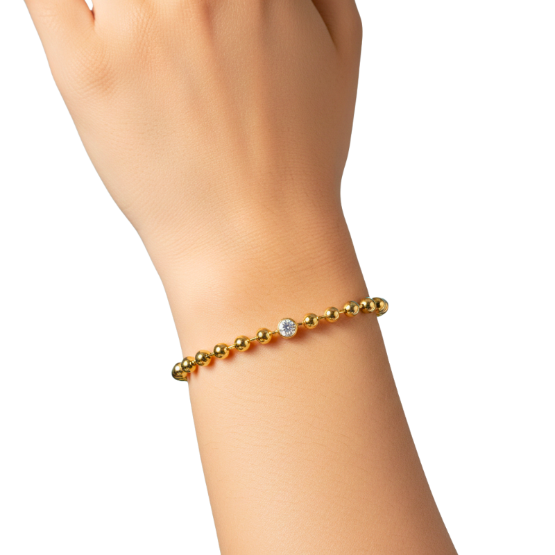 Gold bracelet with a clear gemstone on a wrist against a white background