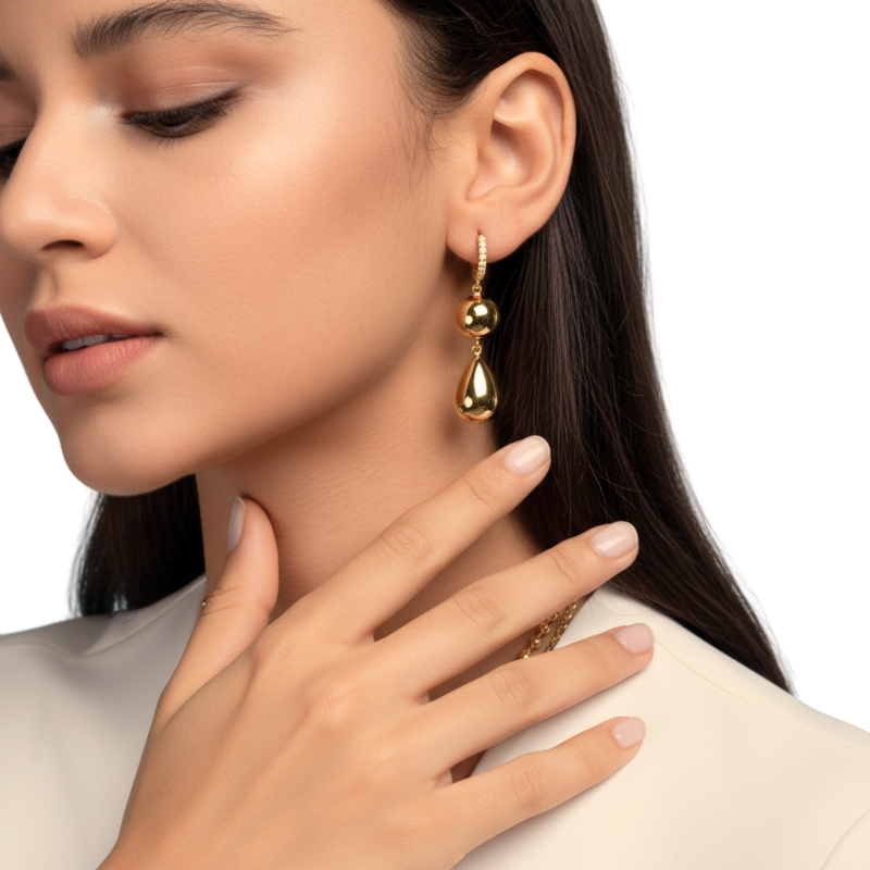 Close-up of a woman wearing gold teardrop earrings with a plain background