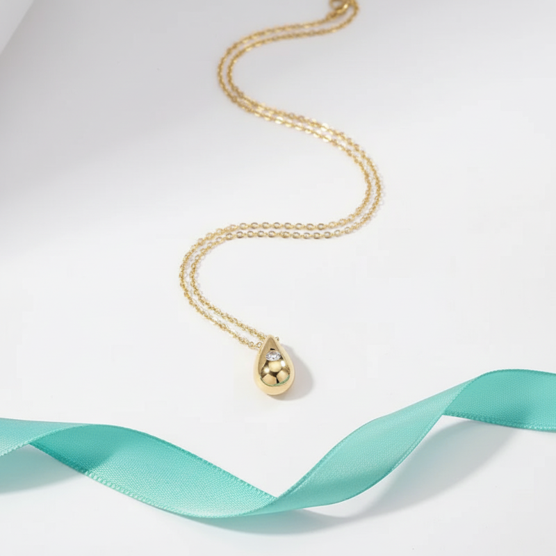 Gold necklace with a teardrop pendant on a light blue ribbon against a white background