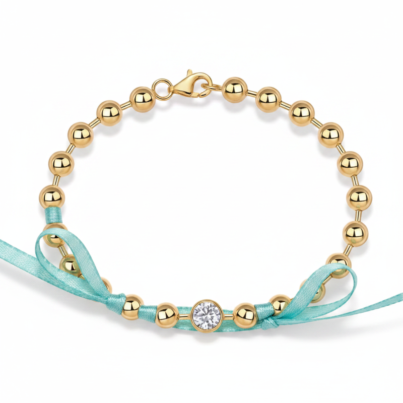 Gold beaded bracelet with a turquoise ribbon on a white background