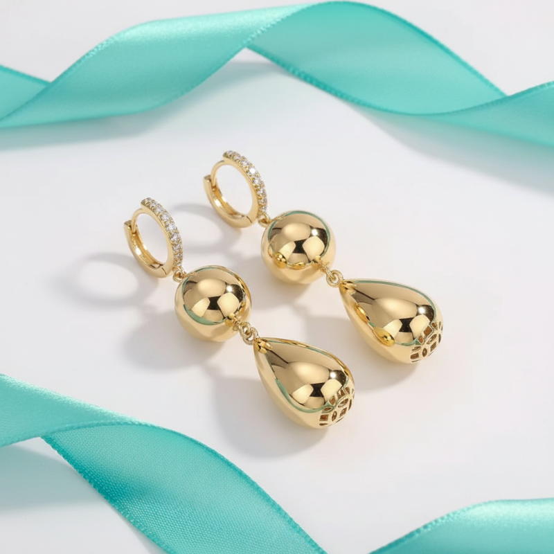 Gold earrings with teardrop design on a light blue ribbon background