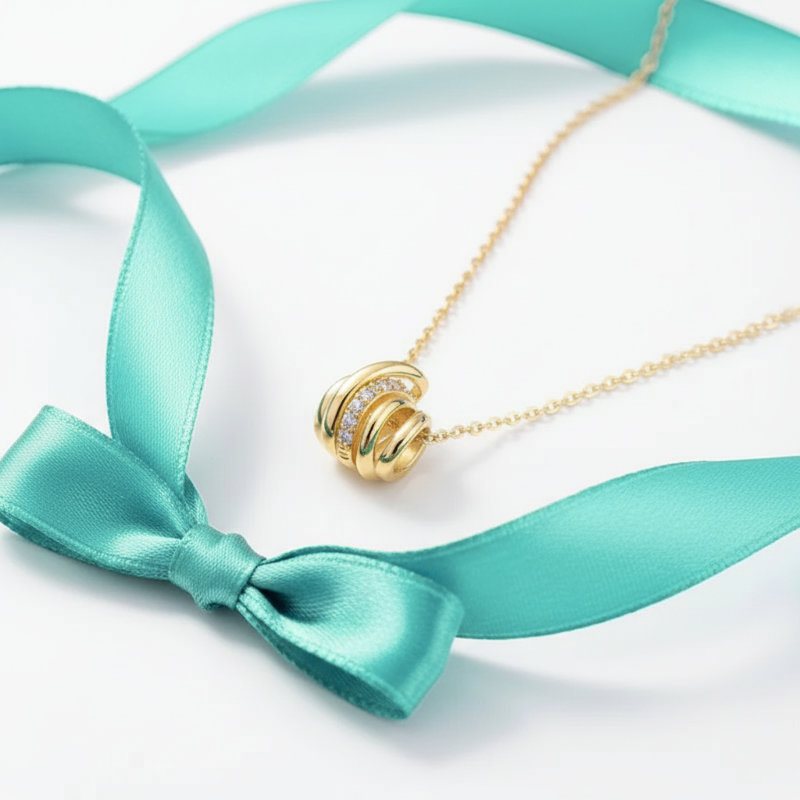 Gold necklace with a bow-shaped pendant on a turquoise ribbon against a white background