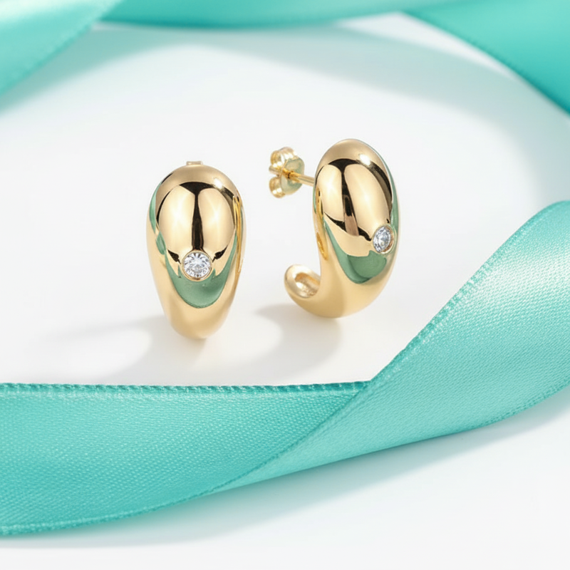 Gold hoop earrings with green accents on a turquoise fabric background