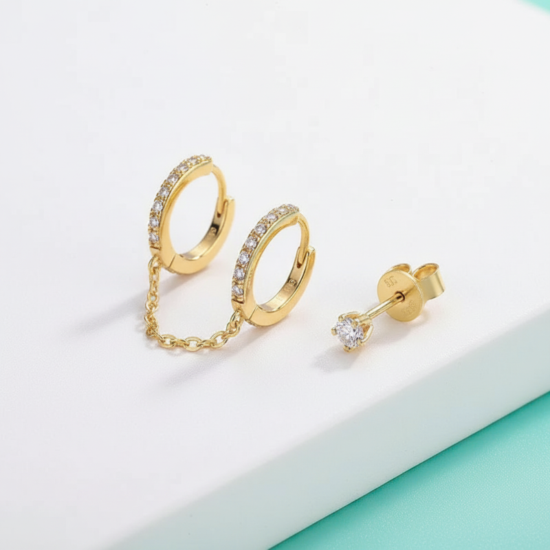 Gold hoop earrings with chain detail and a single stud earring on a light background