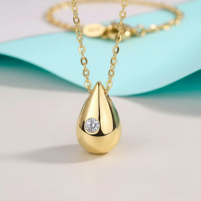 Gold teardrop-shaped pendant with a diamond on a light blue background