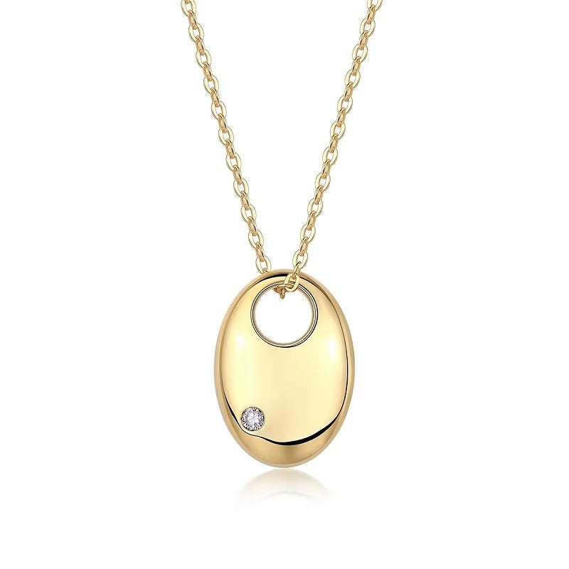 Gold necklace with a round pendant featuring a small diamond on a white background